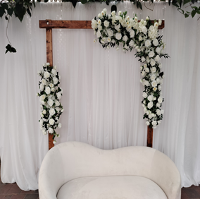 white sheer or voile backdrop with wooden arch and floral arrangement and white velvet couch available in variety of colors used for types for your event wedding birthday ceremony party anniversary, available for rental, rent buy or sale